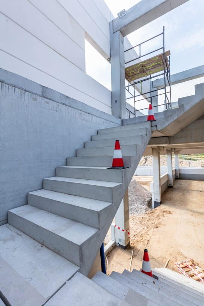 Concrete staircase under construction with safety cones and scaffolding.